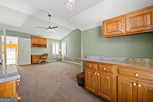 kitchen featuring brown cabinetry, vaulted ceiling, carpet, and built in study area