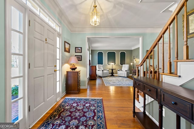 foyer entrance featuring stairway, wood finished floors, baseboards, an inviting chandelier, and crown molding