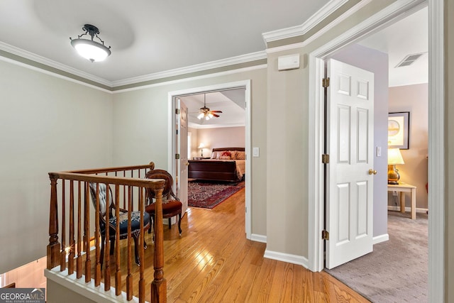 hall with visible vents, baseboards, light wood-style floors, and crown molding