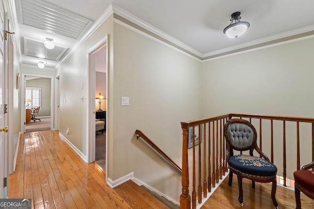 hallway with baseboards, attic access, ornamental molding, light wood-style floors, and an upstairs landing