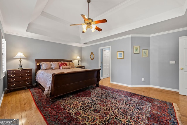 bedroom featuring a raised ceiling, crown molding, wood finished floors, and baseboards