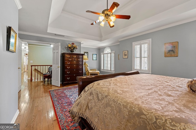 bedroom with visible vents, ceiling fan, crown molding, wood-type flooring, and a raised ceiling