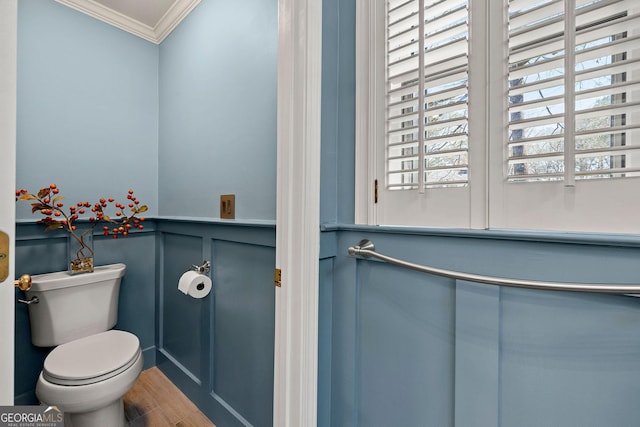 bathroom featuring a wainscoted wall, toilet, ornamental molding, wood finished floors, and a decorative wall