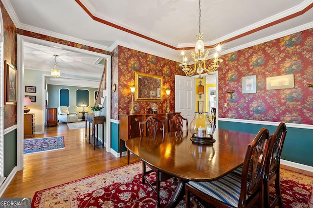 dining area featuring wood finished floors, baseboards, wallpapered walls, crown molding, and a chandelier