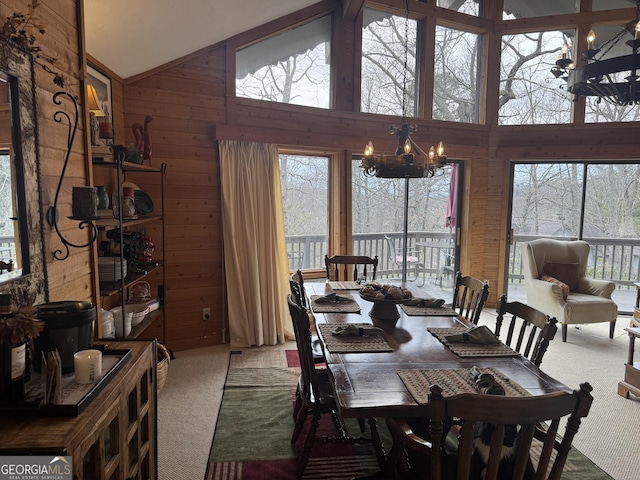 dining area with high vaulted ceiling, a notable chandelier, wood walls, and carpet flooring