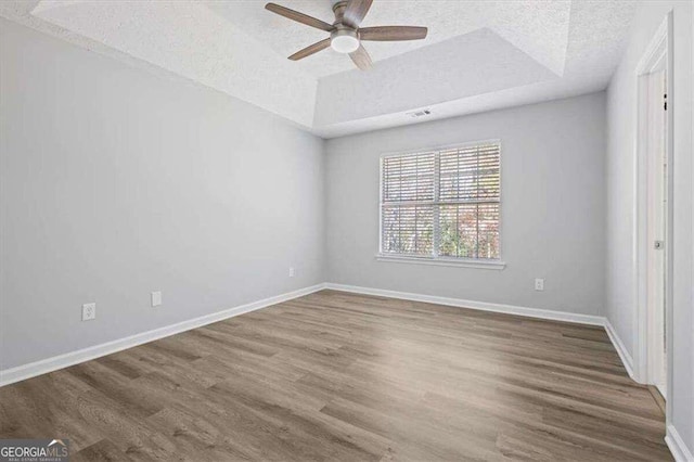 unfurnished bedroom featuring a ceiling fan, wood finished floors, baseboards, a tray ceiling, and a textured ceiling