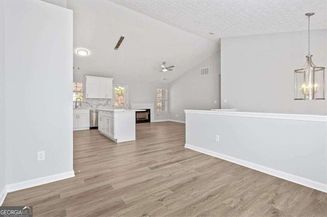 unfurnished living room featuring light wood-type flooring, visible vents, vaulted ceiling, and ceiling fan with notable chandelier