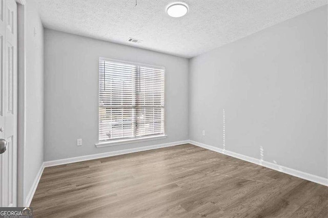 spare room featuring visible vents, baseboards, a textured ceiling, and wood finished floors