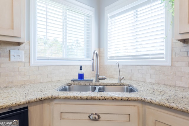 kitchen with tasteful backsplash, a healthy amount of sunlight, light stone countertops, and a sink