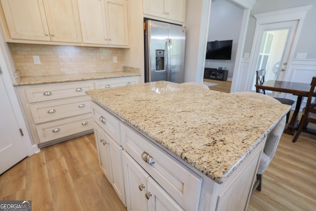 kitchen with a kitchen island, stainless steel fridge, light wood finished floors, decorative backsplash, and light stone countertops