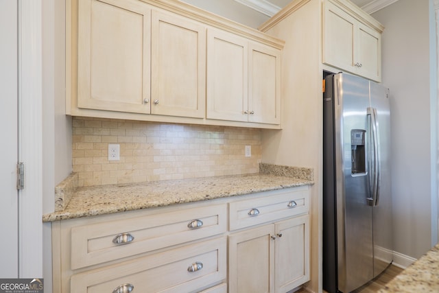 kitchen with ornamental molding, stainless steel refrigerator with ice dispenser, light stone counters, tasteful backsplash, and baseboards