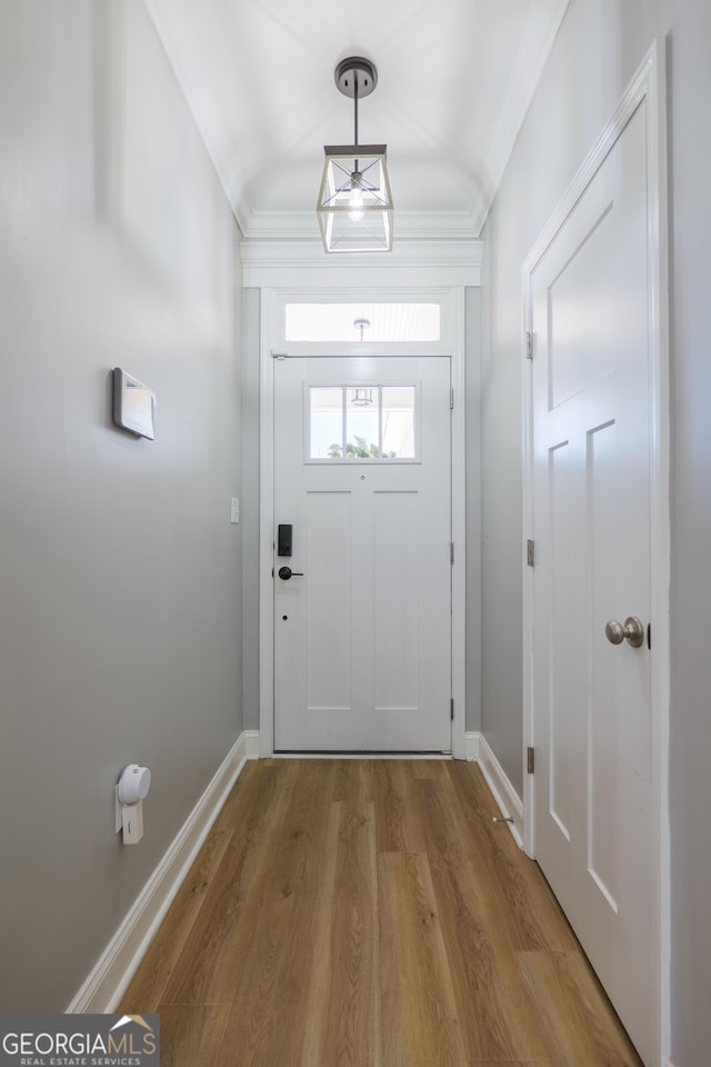 doorway to outside with wood finished floors, baseboards, and ornamental molding