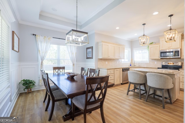 dining area featuring a wainscoted wall, a raised ceiling, light wood-style floors, and ornamental molding