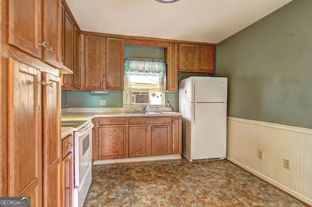 kitchen with a sink, white appliances, brown cabinetry, wainscoting, and light countertops