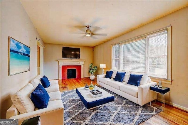 living area featuring baseboards, a fireplace, wood finished floors, and a ceiling fan