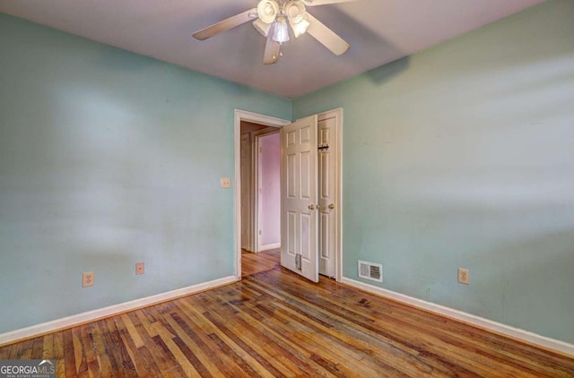 unfurnished room with hardwood / wood-style floors, visible vents, baseboards, and ceiling fan