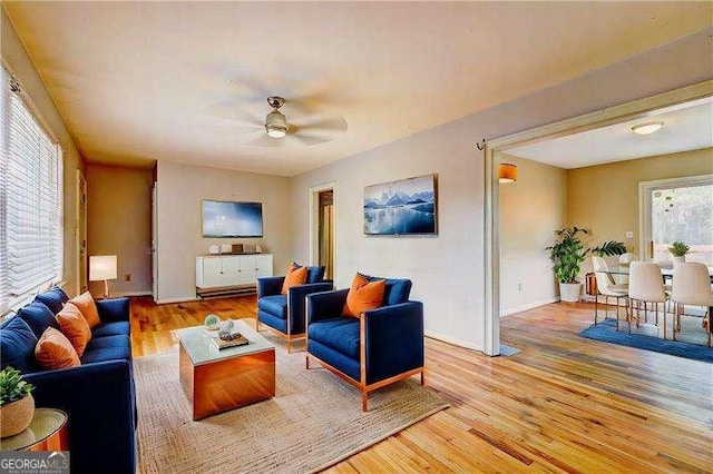 living area featuring light wood-style flooring, baseboards, and ceiling fan