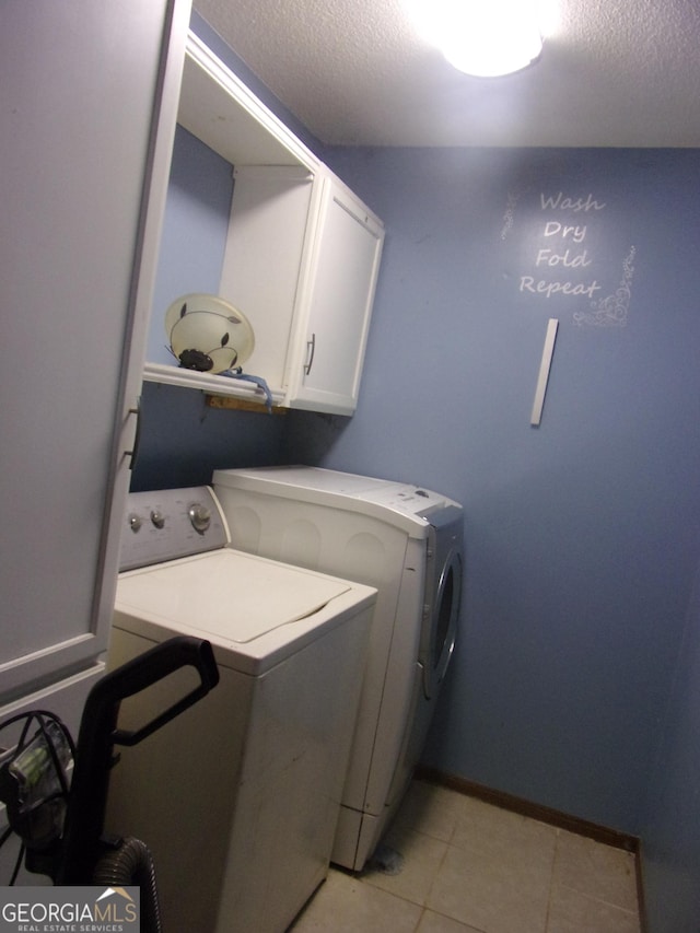 laundry area with light tile patterned floors, baseboards, washing machine and clothes dryer, cabinet space, and a textured ceiling