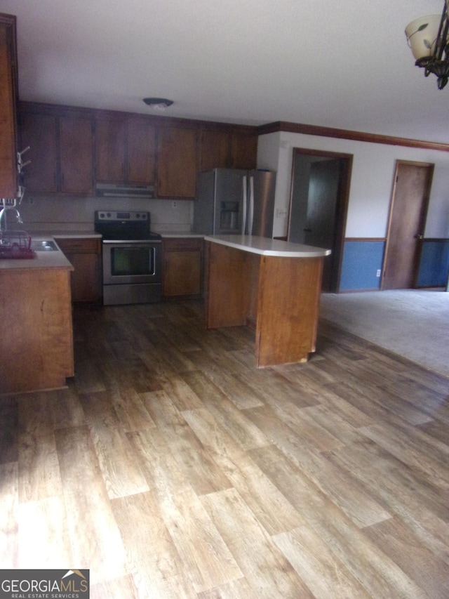 kitchen featuring a kitchen island, appliances with stainless steel finishes, wood finished floors, brown cabinetry, and a sink