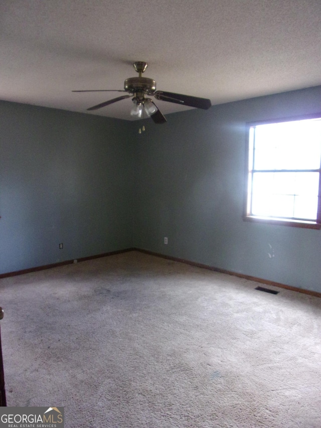 carpeted empty room with ceiling fan, baseboards, visible vents, and a textured ceiling