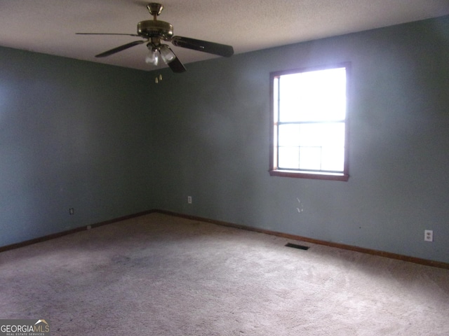 carpeted spare room with visible vents, baseboards, and a ceiling fan