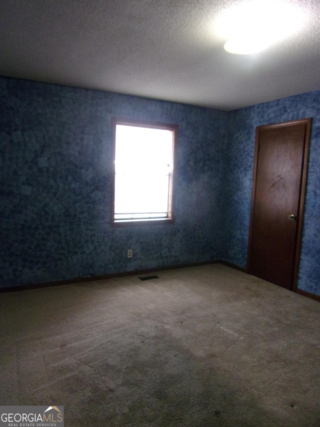 carpeted empty room with visible vents and a textured ceiling