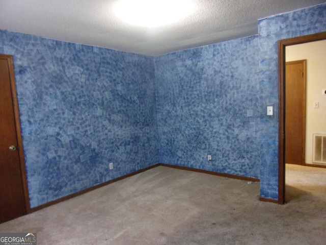 unfurnished room with visible vents, a textured ceiling, wallpapered walls, and carpet floors