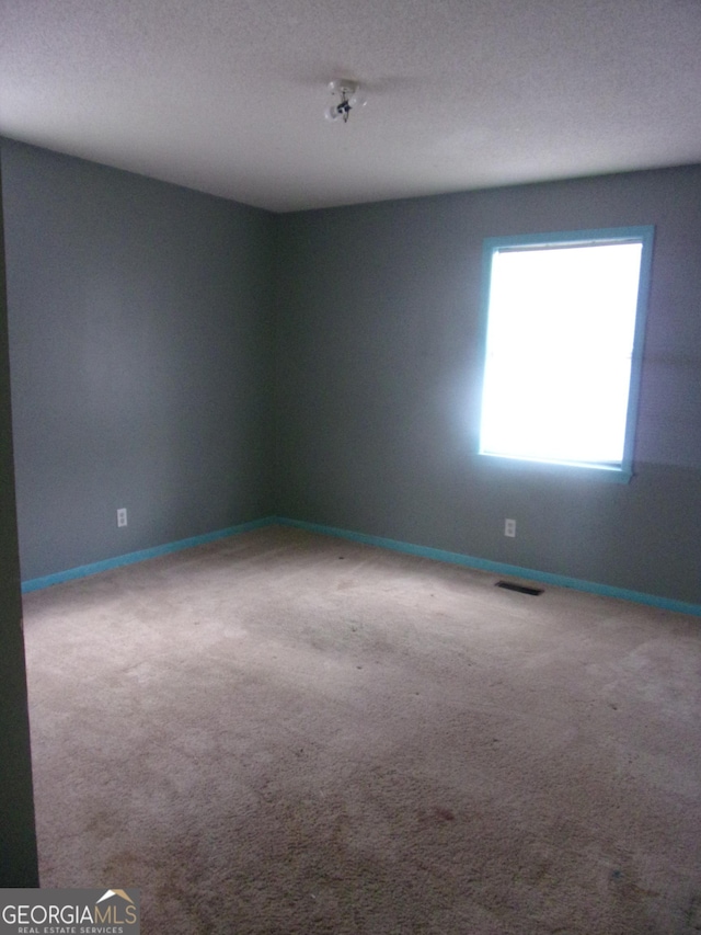 carpeted spare room with visible vents and baseboards