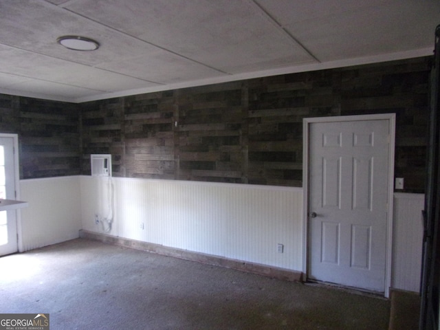 carpeted empty room featuring wainscoting and wood walls