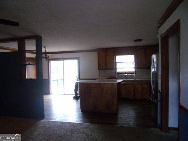 kitchen with dark wood finished floors, a peninsula, freestanding refrigerator, a sink, and light countertops