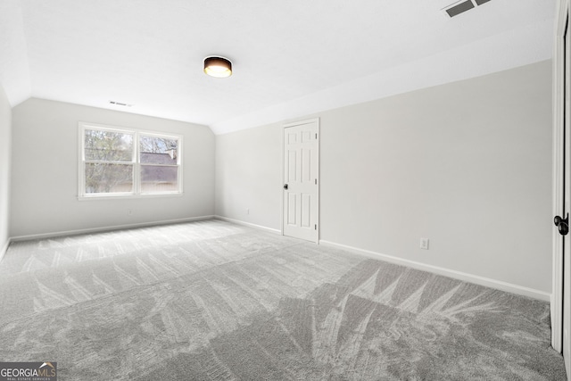 carpeted spare room featuring lofted ceiling, baseboards, and visible vents