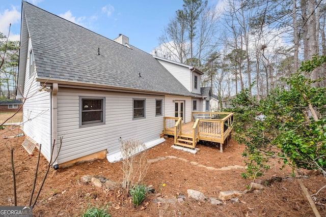 back of house with a wooden deck, a chimney, and a shingled roof