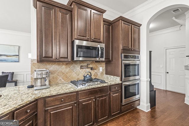 kitchen with light stone countertops, visible vents, arched walkways, ornamental molding, and appliances with stainless steel finishes