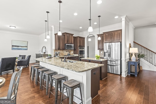 kitchen with a sink, stainless steel appliances, dark brown cabinets, a kitchen bar, and a center island