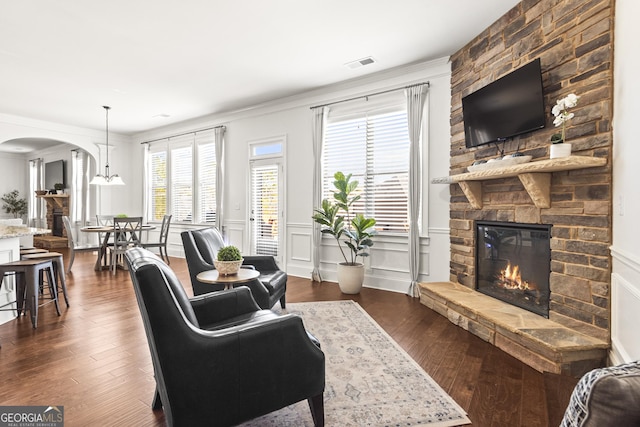 living room featuring dark wood-style floors, visible vents, arched walkways, and a stone fireplace