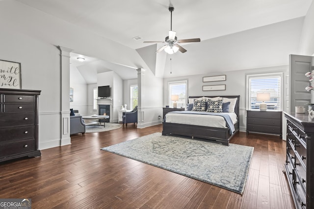 bedroom featuring a glass covered fireplace, dark wood-type flooring, decorative columns, and lofted ceiling