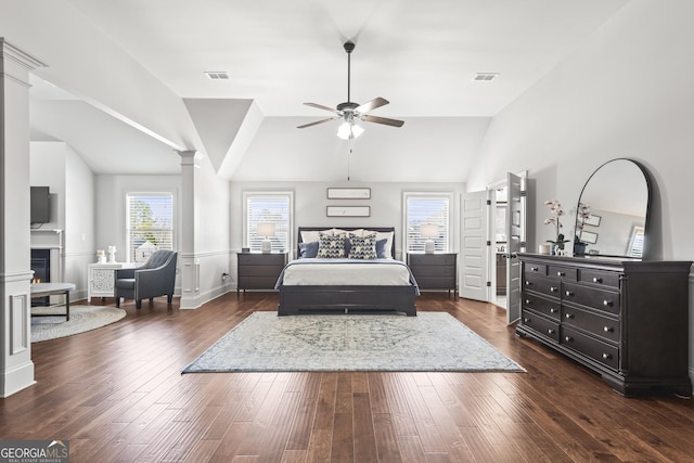 bedroom with visible vents, a warm lit fireplace, dark wood finished floors, decorative columns, and lofted ceiling