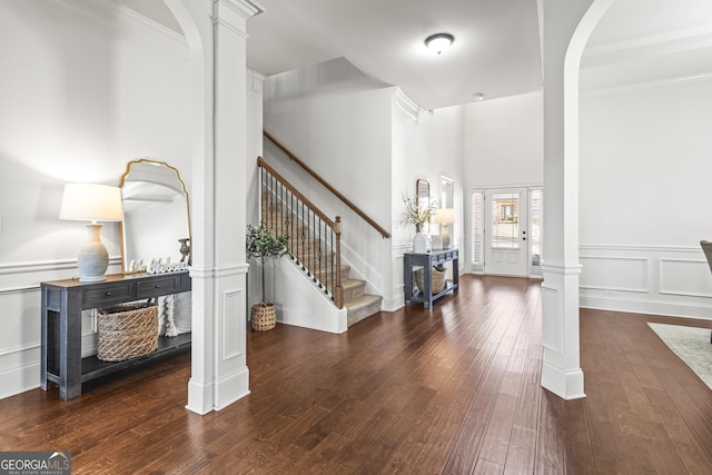 foyer featuring hardwood / wood-style floors, stairway, decorative columns, arched walkways, and a decorative wall