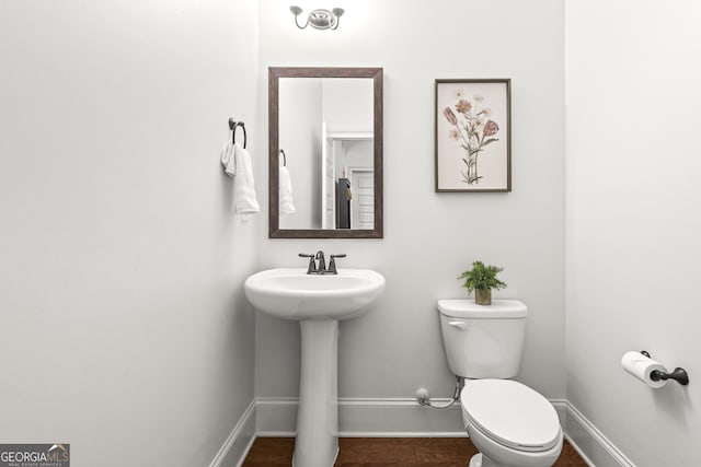 half bathroom with toilet, baseboards, and a sink