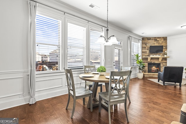 dining space with visible vents, hardwood / wood-style flooring, a stone fireplace, crown molding, and a decorative wall