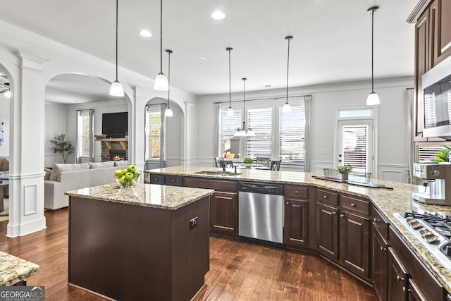 kitchen with crown molding, a stone fireplace, arched walkways, stainless steel appliances, and a sink