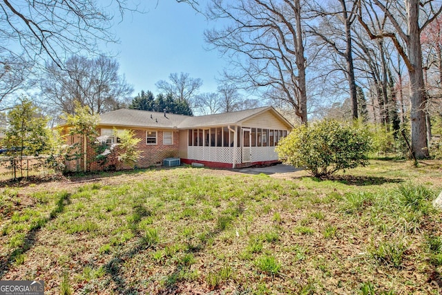 rear view of property with brick siding, central AC unit, a yard, and a sunroom