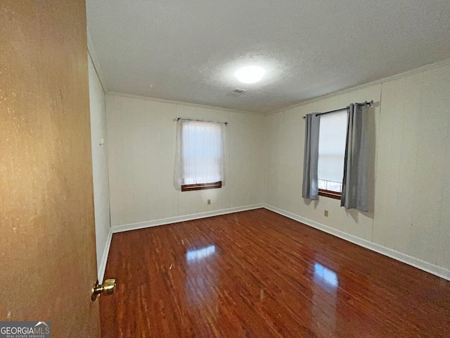 empty room with a textured ceiling, crown molding, baseboards, and wood finished floors