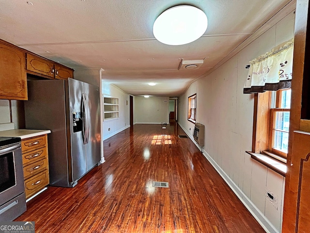 kitchen featuring heating unit, brown cabinetry, visible vents, dark wood-type flooring, and appliances with stainless steel finishes