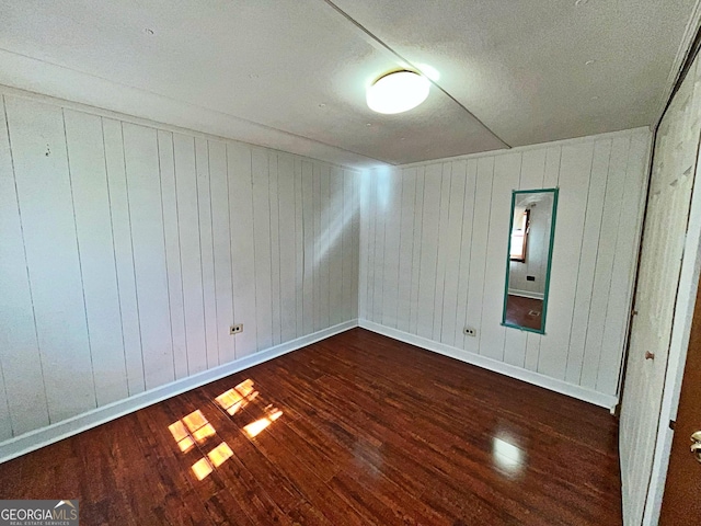 spare room with baseboards and dark wood-type flooring