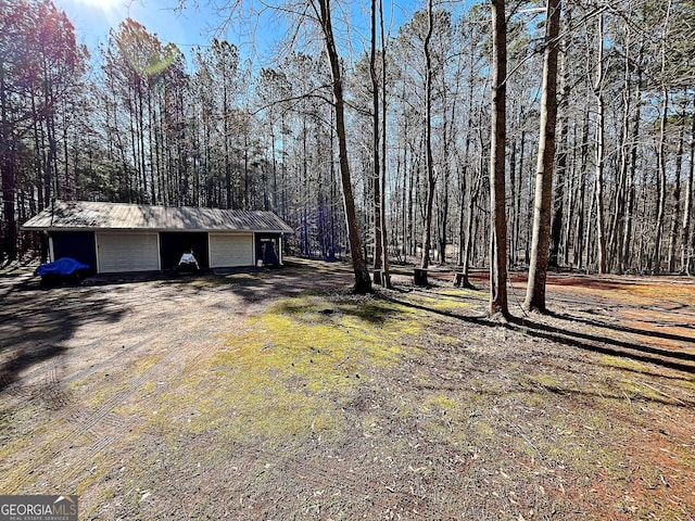 view of yard featuring a garage, a forest view, an outdoor structure, and dirt driveway