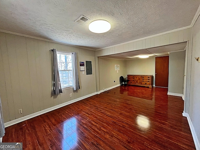 empty room featuring visible vents, ornamental molding, electric panel, hardwood / wood-style floors, and baseboards