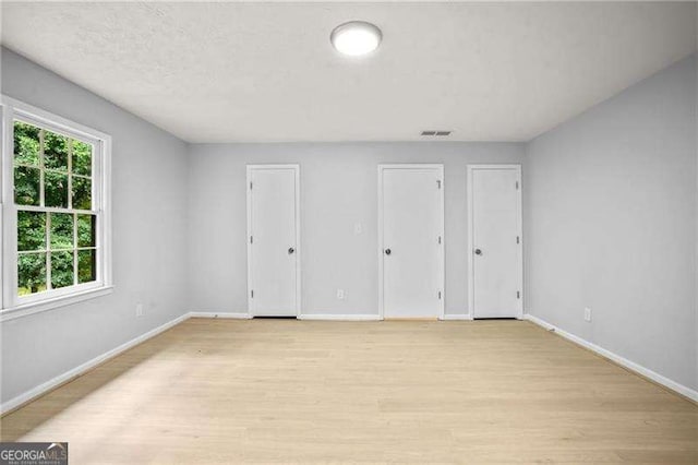 unfurnished bedroom featuring visible vents, baseboards, two closets, and light wood finished floors