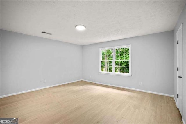 empty room featuring visible vents, baseboards, light wood-style floors, and a textured ceiling