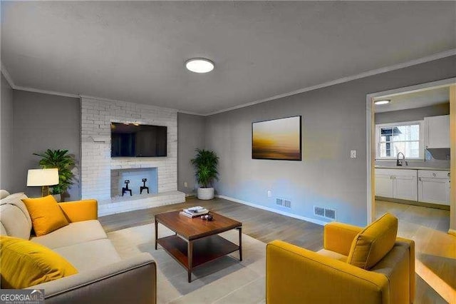 living room featuring light wood finished floors, visible vents, a brick fireplace, and crown molding